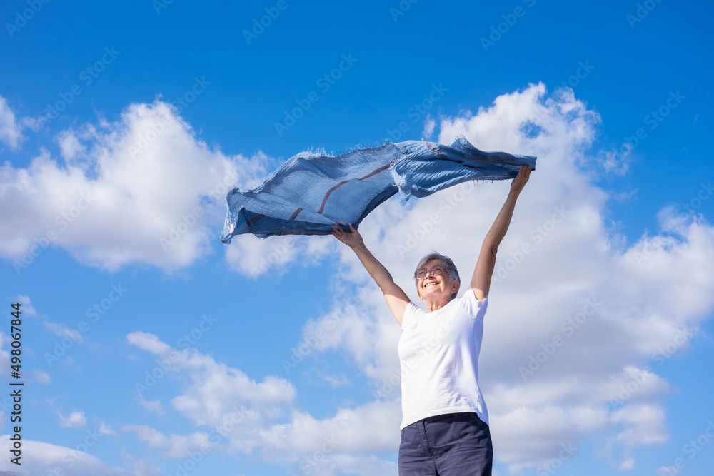 Happy mature elderly woman outdoors waving scarf in the wind. Smiling caucasian elderly woman with short hair wearing glasses enjoying freedom and vacation Happy mature elderly woman outdoors waving scarf in the wind. Smiling caucasian elderly woman with short hair wearing glasses enjoying freedom and vacation