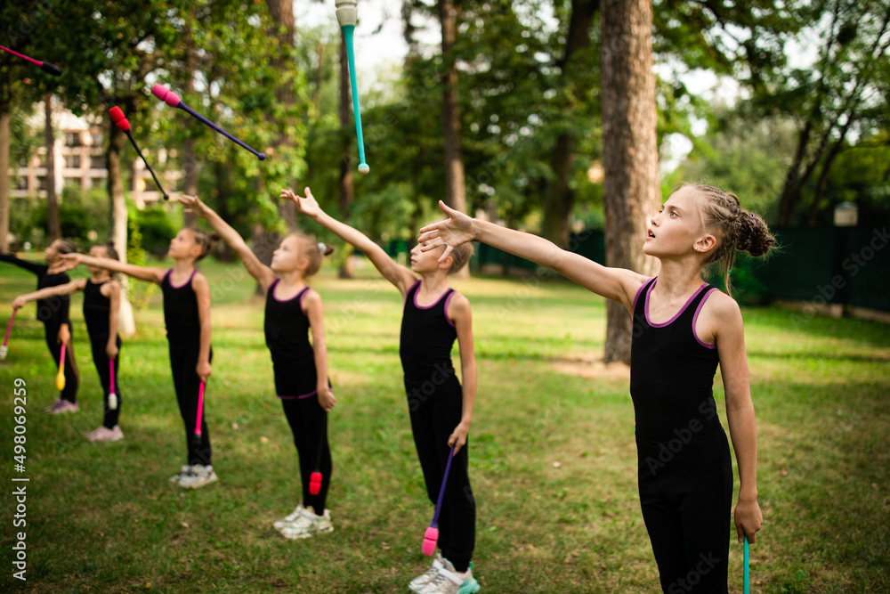 Girls gymnasts doing exercise with clubs together on rhythmic gymnastics training in summer sports camp