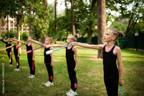 Girls gymnasts doing exercise with clubs together on rhythmic gymnastics training in summer sports camp © Olena Shvets