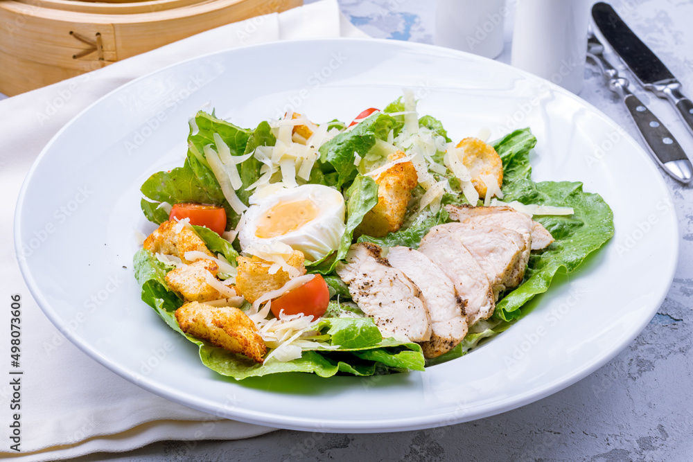 Salad caesar with chicken on white plate on grey table Salad caesar with chicken on white plate on grey table