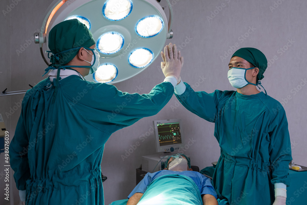 Portrait shot of doctor and assistance nurse wearing surgical coat while doing surgical operation for patient inside of the hospital. Medical and professional service occupation.