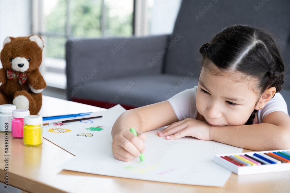 ํYoung girl sit on the sofa while using water color and crayon to paint on the paper inside of the living room. Children creativity and learning process, art and education for kids ํYoung girl sit on the sofa while using water color and crayon to paint on the paper inside of the living room. Children creativity and learning process, art and education for kids