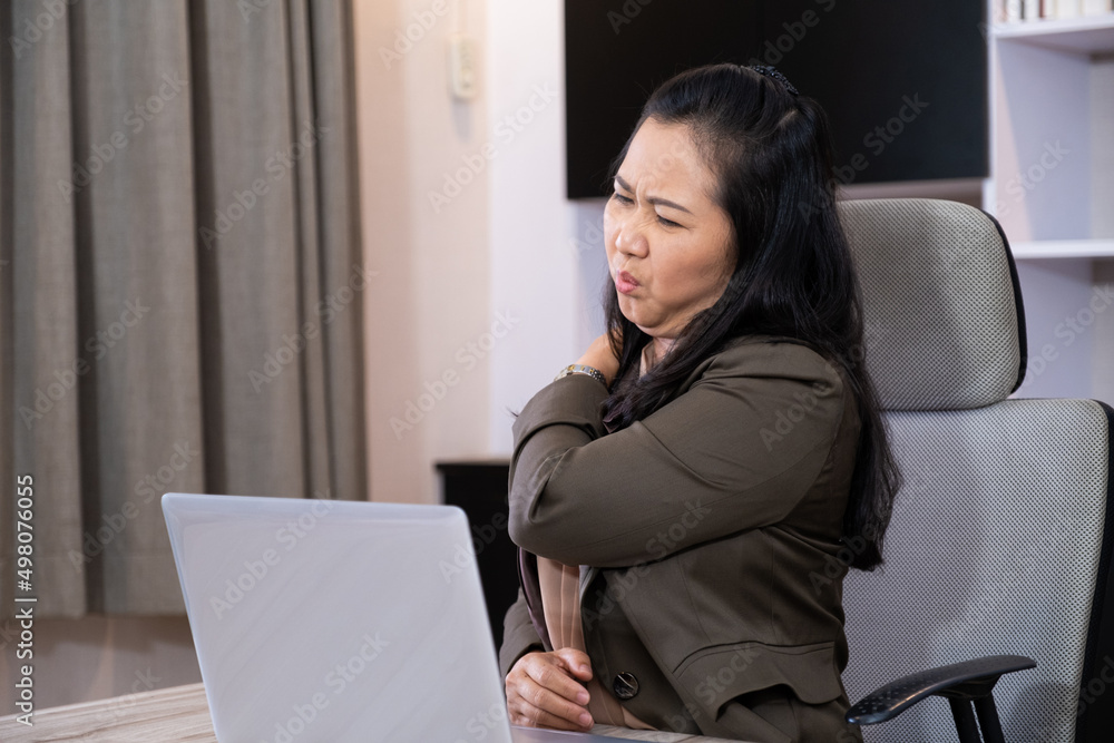 Adult business women feeling painful from back and shoulder ache while working, online meeting in front of the computer inside of the office area. Office syndrome, over working illness.