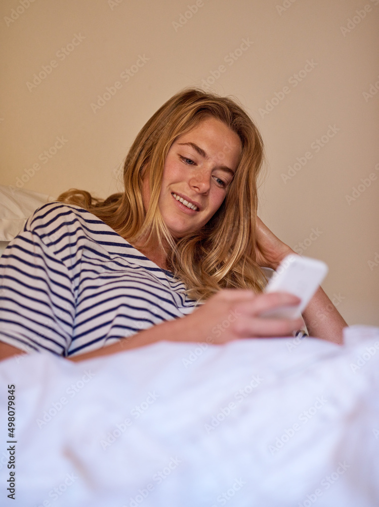 What are my friends doing today. Shot of a happy young woman using her cellphone while lying in bed. What are my friends doing today. Shot of a happy young woman using her cellphone while lying in bed.