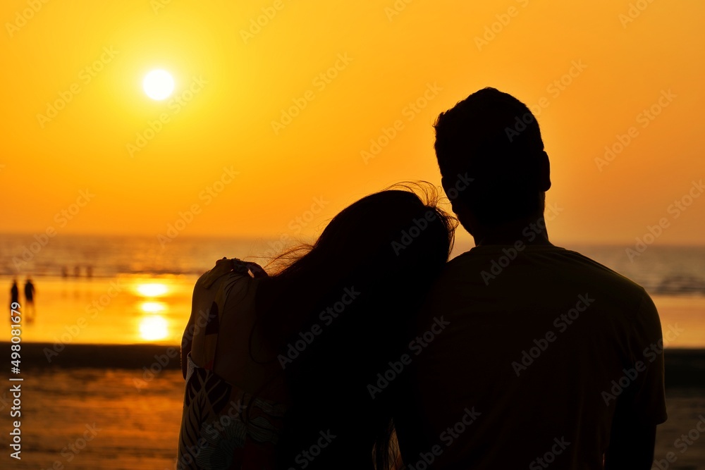A beautiful silhouette of a couple enjoying their quality time at a beach during sunset. Love, life, hug, kiss, marriage, engagement, propose, romance concept