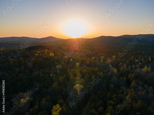 Forest with rolling hills and mountains. Mountains in the background show the landscape. The sunset golden hour creates a golden hue atmosphere on the trees and mountains. © Jeremy