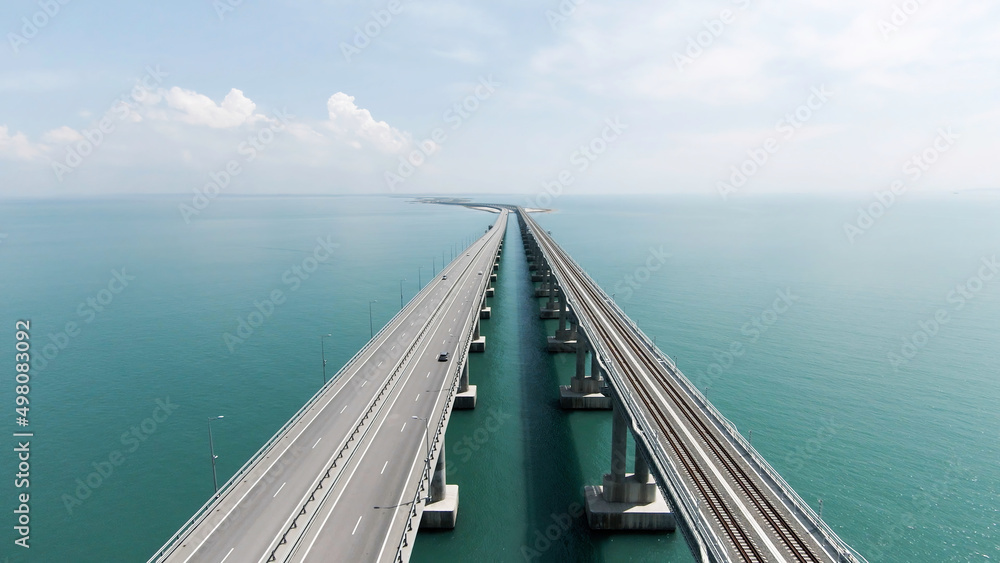 Aerial view along the long beautiful bridge above turquoise sea. Action. Flying above bending bridge with driving cars. - obrazy, fototapety, plakaty 
