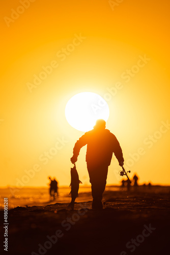 Silhouette of a fisherman carrying a large fish back from the beach at sunset. Jones Beach, Long Island New York