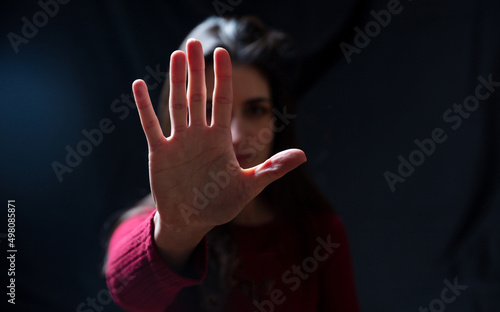 Stop violence against women. Young woman with raised hand for dissuade, black background, space photo