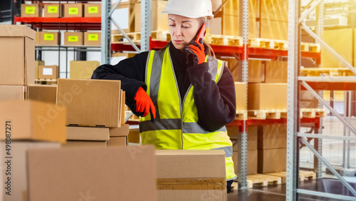 Sorting center employee. Woman worker sorting warehouse. Warehouse worker talking on phone. Girl with mobile phone. Warehouse worker call customer. Fulfillment company. Girl in yellow vest with boxes