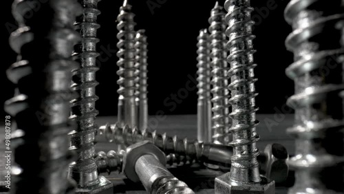 Screws, metal threaded bolts, fasteners on table on isolated black background. Steel chrome anchor screws in workshop or hardware shop. Super macro close up of fixing tools. Slow motion ready 59.97fps
