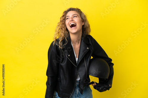 Young blonde woman with a motorcycle helmet isolated on yellow background laughing © luismolinero