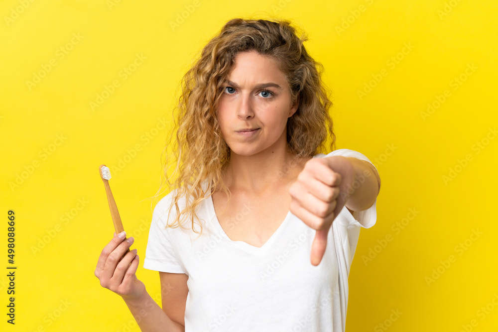 Young caucasian woman holding a brushing teeth isolated on yellow background showing thumb down with negative expression Young caucasian woman holding a brushing teeth isolated on yellow background showing thumb down with negative expression