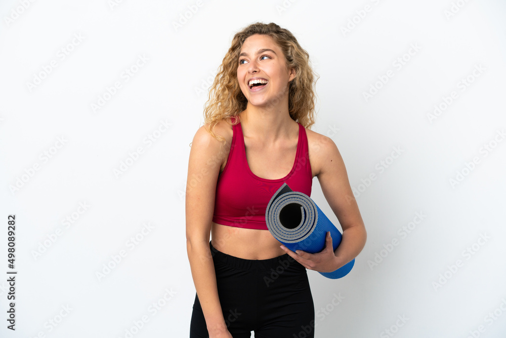 Young sport blonde woman going to yoga classes while holding a mat isolated on white background looking to the side and smiling Young sport blonde woman going to yoga classes while holding a mat isolated on white background looking to the side and smiling