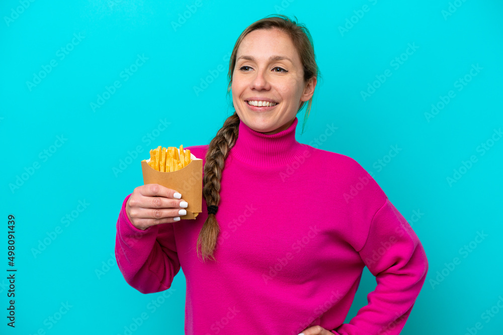 Young caucasian woman holding fried chips isolated on blue background posing with arms at hip and smiling Young caucasian woman holding fried chips isolated on blue background posing with arms at hip and smiling