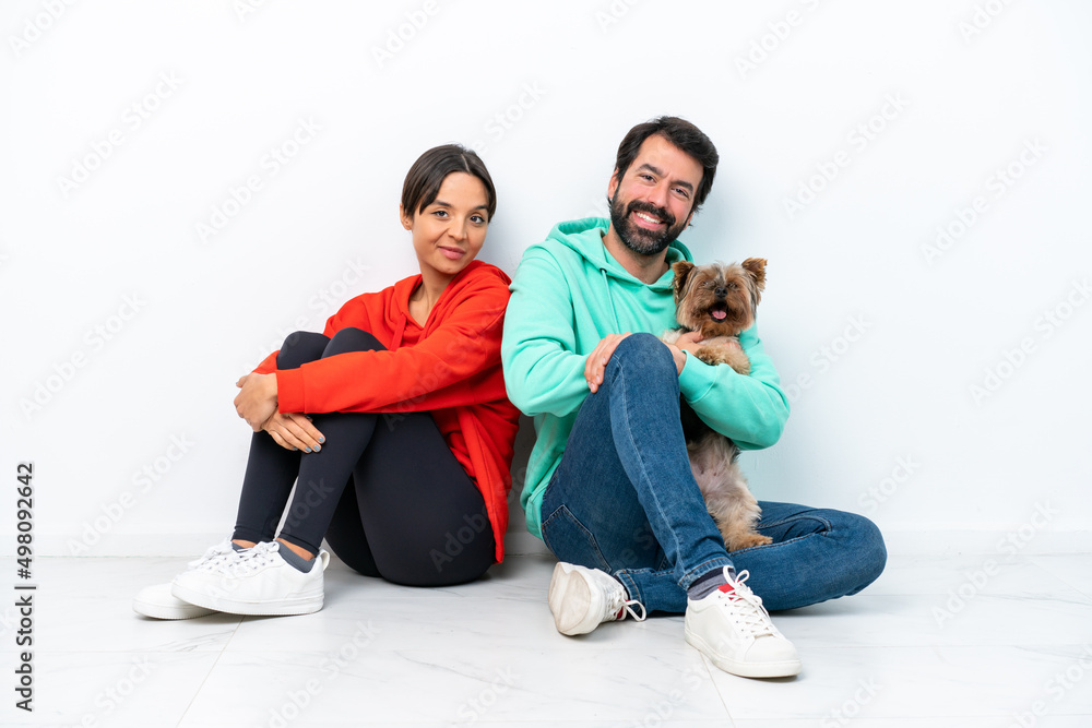Young caucasian couple sitting on the floor with their pet isolated on white background keeping arms crossed Young caucasian couple sitting on the floor with their pet isolated on white background keeping arms crossed
