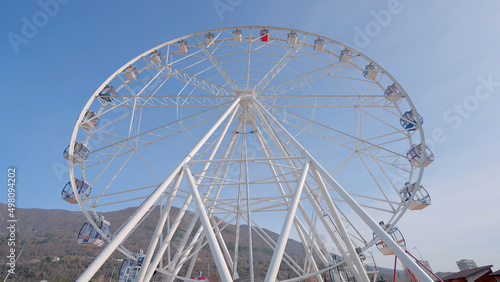 A ferris wheel at the amusement park at daytime. Action. Bottom view of white romantic attraction on blue sky background. photo