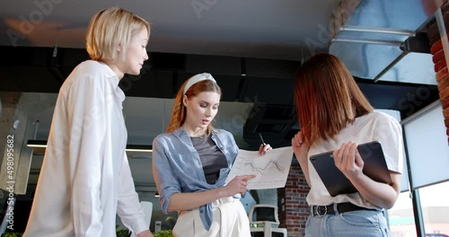 Working team of women standing over the table and charts and discussing project. IT employees. Females talking and brainstorming. Startup concept. Coworking and planning business in numbers. photo