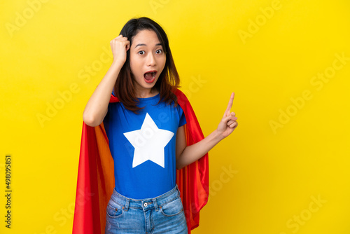 Super hero Vietnamese woman isolated on yellow background surprised and pointing finger to the side