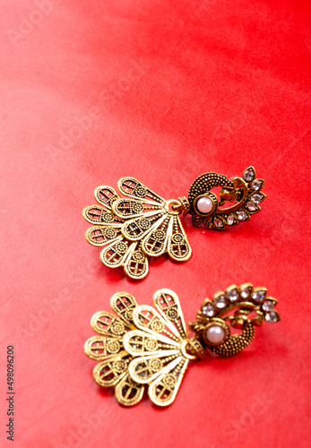"Closeup of pair of beautiful peacock shaped earrings on colorful background"