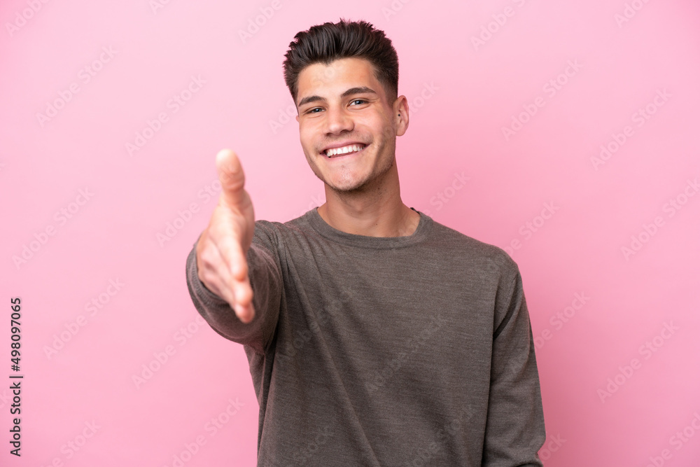 Young caucasian man isolated on pink background shaking hands for closing a good deal Young caucasian man isolated on pink background shaking hands for closing a good deal