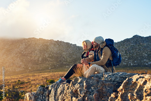 The best view comes from the hardest climb. Shot of two hikers sitting on top of a mountain having a conversation. photo