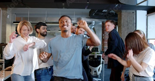 Mixed-races men and women celebrating end of working week in office. Multiethnic coworkers dancing and having fun ar workplace. Young team of company employees having party. photo