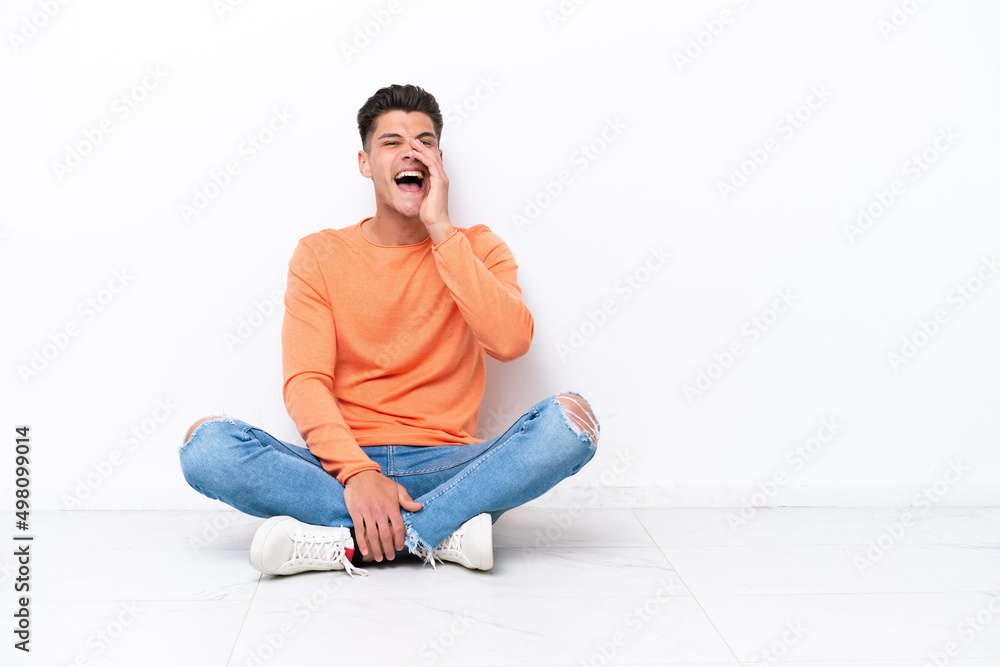 Young man sitting on the floor isolated on white background shouting with mouth wide open