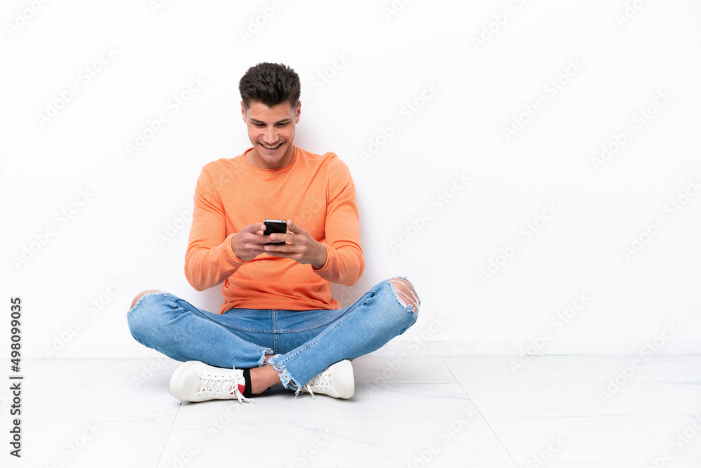 Young man sitting on the floor isolated on white background sending a message with the mobile Young man sitting on the floor isolated on white background sending a message with the mobile