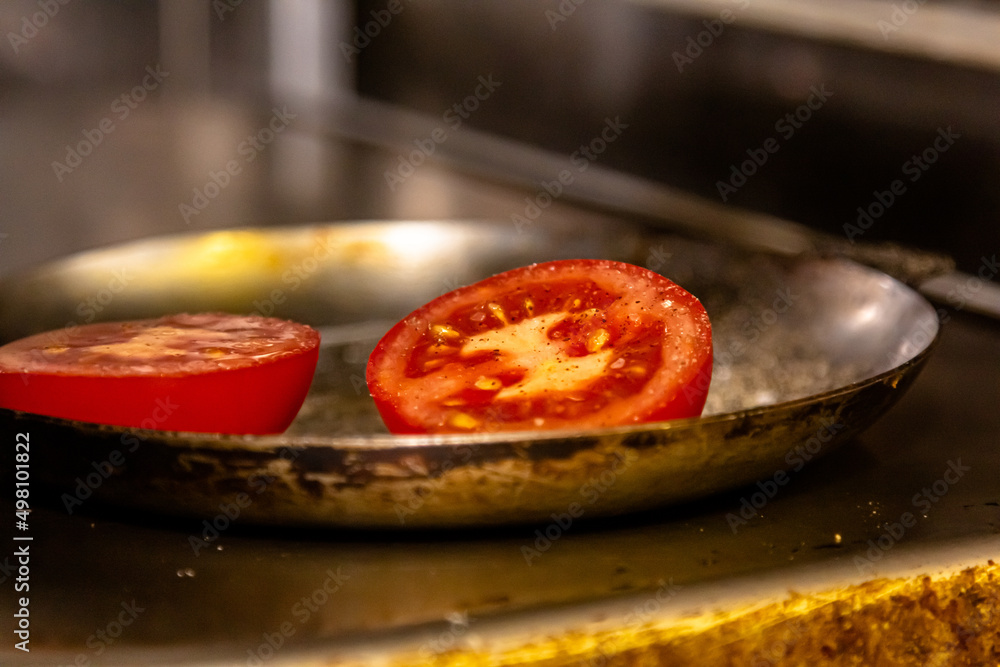 Tomato halves are fried in a steel frying pan Tomato halves are fried in a steel frying pan