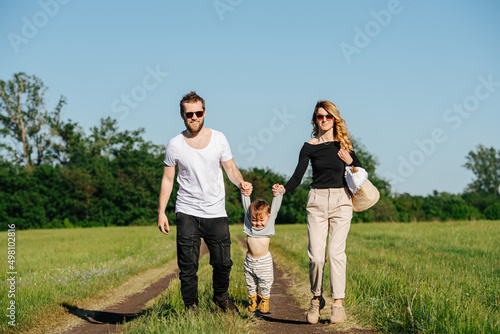 Happy young family walking on spring grass field in a countryside, lifting baby