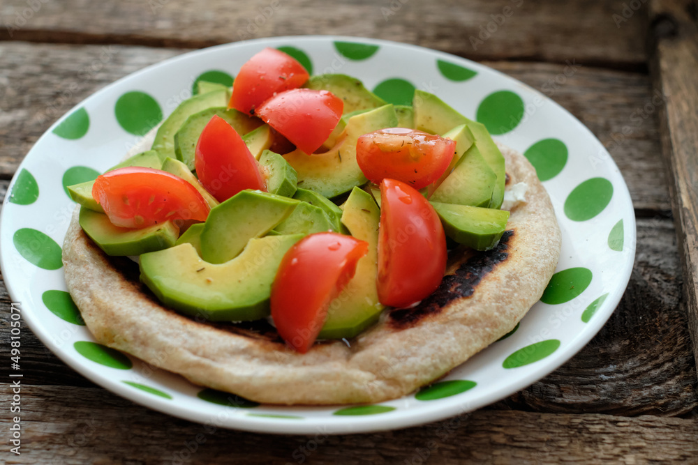 Flatbread with avocado and tomato. Wooden background, side view Flatbread with avocado and tomato. Wooden background, side view