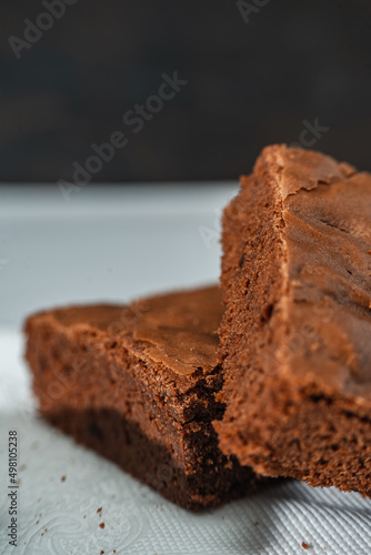 Close up of cubes of chocolate brownies on a white plate on a marble table. copy space.