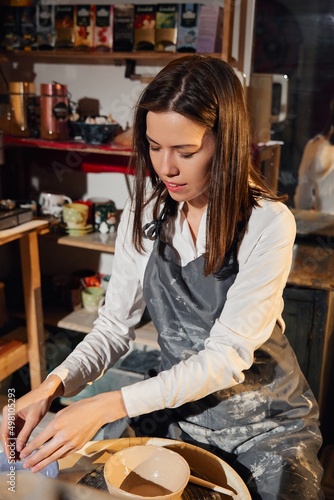 Portrait of a girl in a pottery workshop. Beautiful brunette at the potter's wheel.