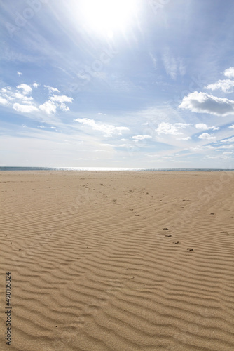 View of empty beach beach with the sea in the background and the sun high in the sky with clouds