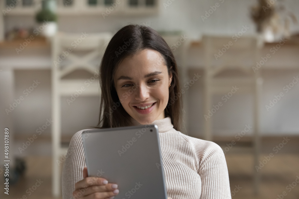 Happy pretty young woman holding tablet computer in home living room, using online app, browsing internet, chatting on social network, reading, making video call, smiling. Communication concept Happy pretty young woman holding tablet computer in home living room, using online app, browsing internet, chatting on social network, reading, making video call, smiling. Communication concept