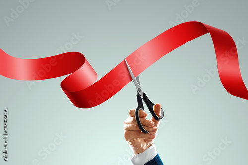Grand opening with red ribbon and scissors. A businessman's hand holds scissors cuts a red ribbon on a light background. Close-up, copy space. photo