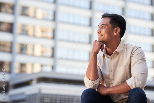 A young Asian businessman sits and looks out over the city smiling