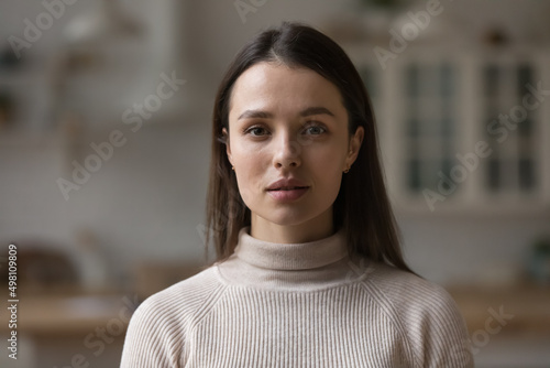 Positive serious millennial model girl home female head shot portrait. Beautiful young adult Caucasian woman looking at camera, posing in apartment. Front profile picture photo