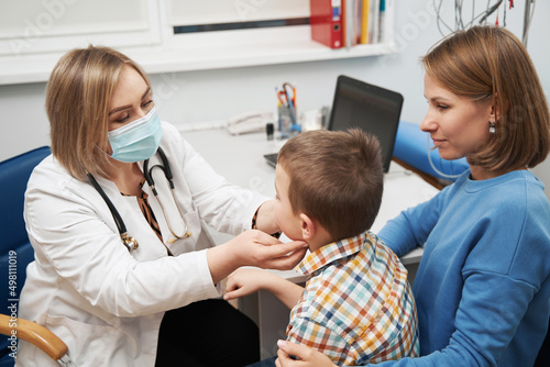 Female pediatrician examining little boy neck in clinic