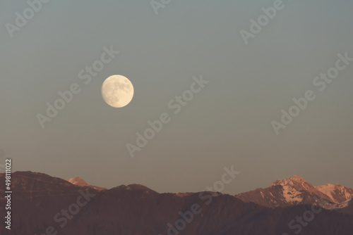 Full moon rises over mountain range evening sky.