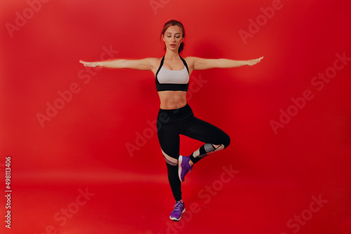 Full-lenght portrait of fit woman with dark hair is dressed in sport uniform is making yoga movement.