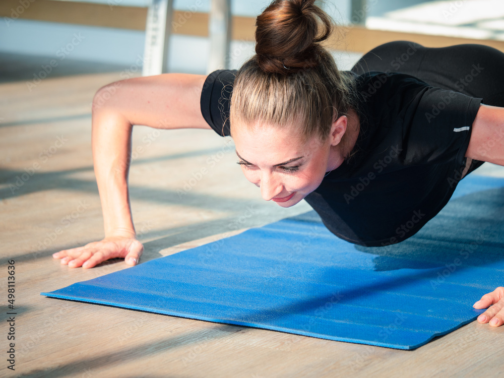 Fototapeta premium Attractive sporty woman doing push-ups at the indoor gym. Sports exercise and muscular build, fitness Women concept.