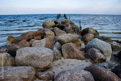 Old wooden poles on the shores of the Baltic Sea with stones in the foreground