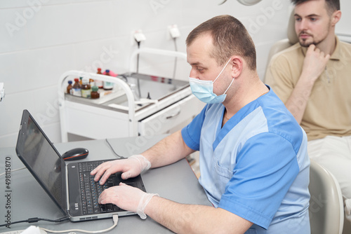 Doctor typing on laptop during appointment with man