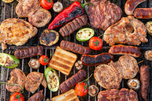 A large variety of grilled meat on the fire outside. Picnic with meat: sausages, pork steak, chicken breast with vegetables. 