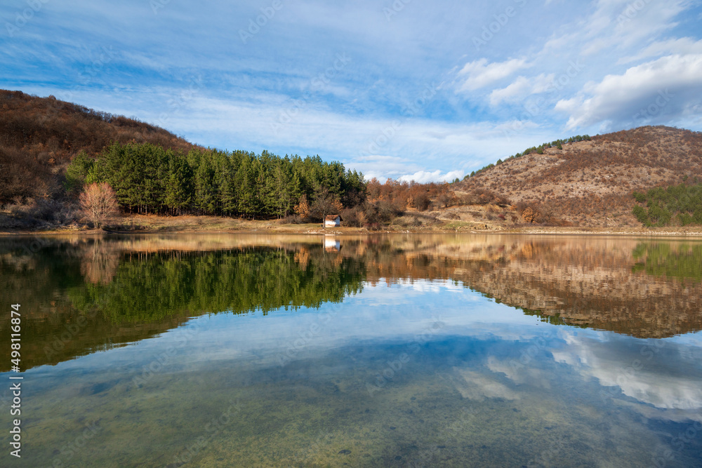 Beautiful mountain landscape and picturesque reflection in the water of the small chapel and forest trees on the shore of the incredible dam in the village of 