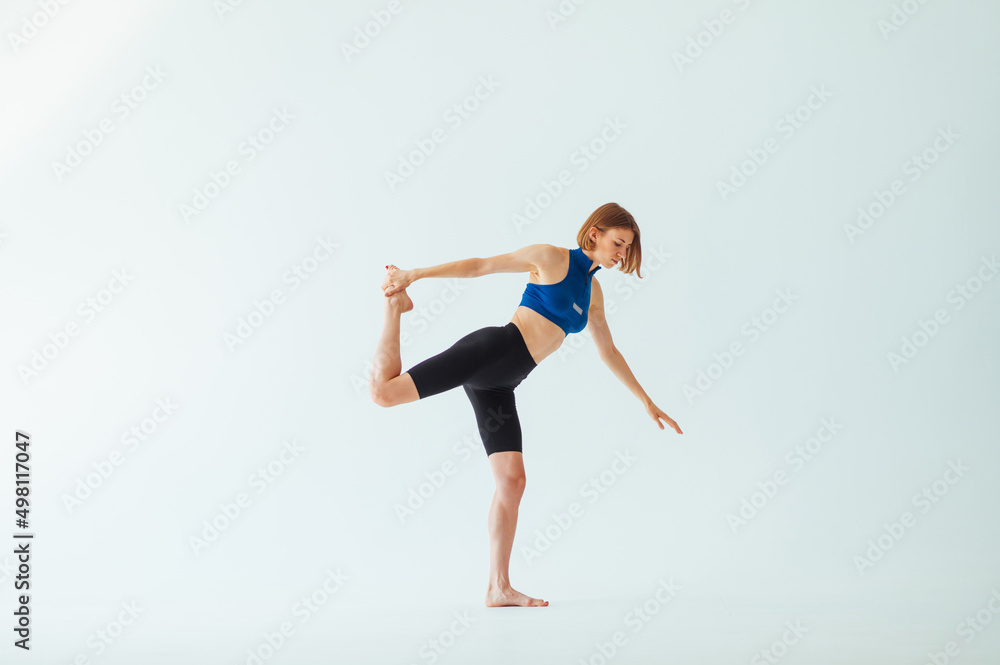 Athletic beautiful woman in a blue top stands on a white background and stretches before training.