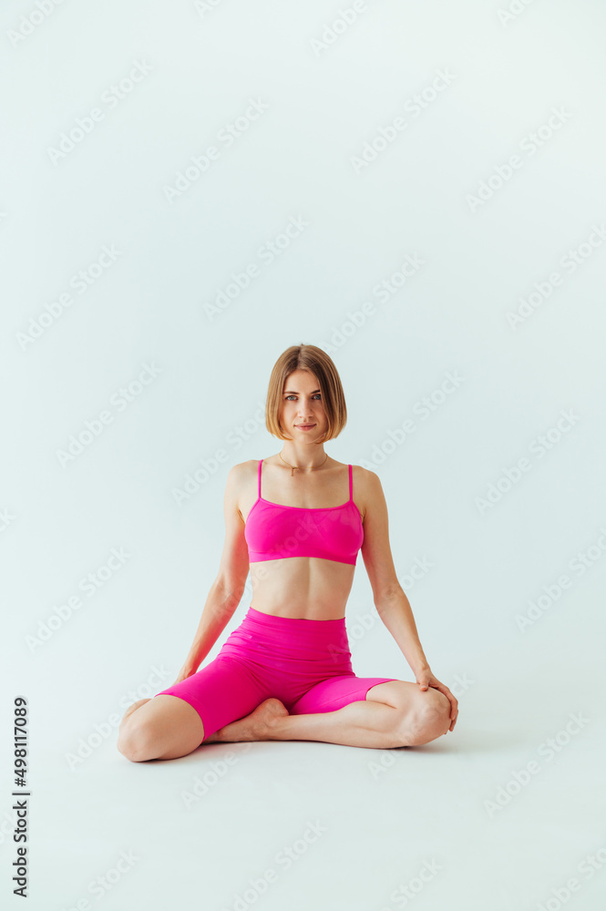 Attractive sports woman in pink clothes sits on a white background and poses for the camera before playing sports.