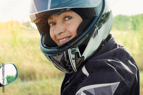 Attractive woman 60 years old in a motorcycle helmet looking at the camera. Close-up portrait. © natavilman